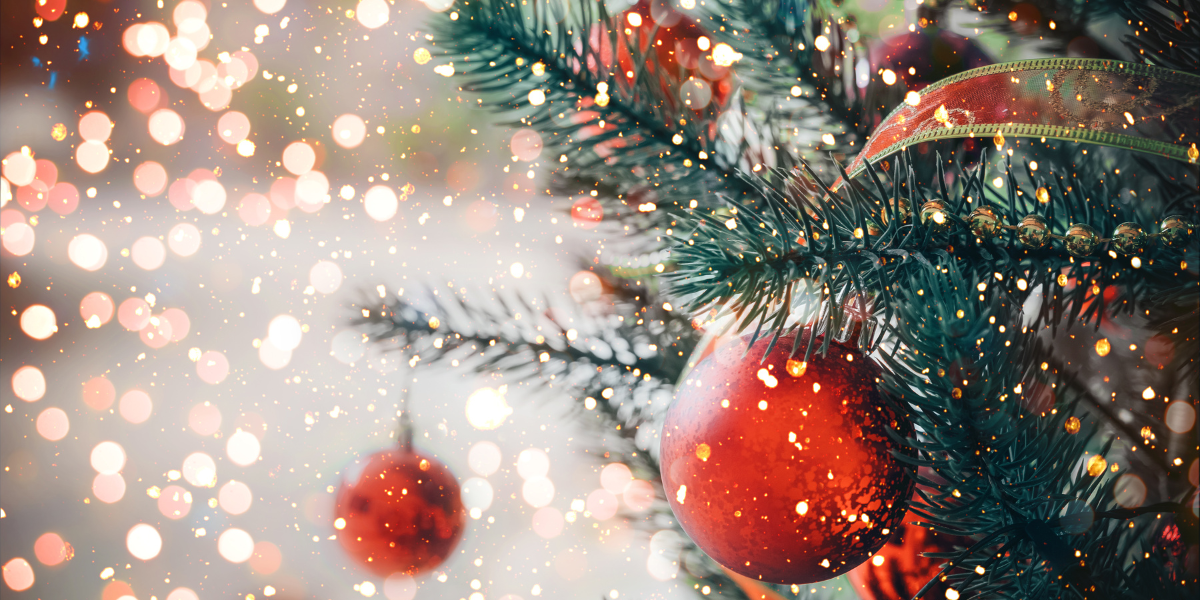 A Christmas tree close-up of branches with ornaments and various decor. Sparkles and lights dust the image